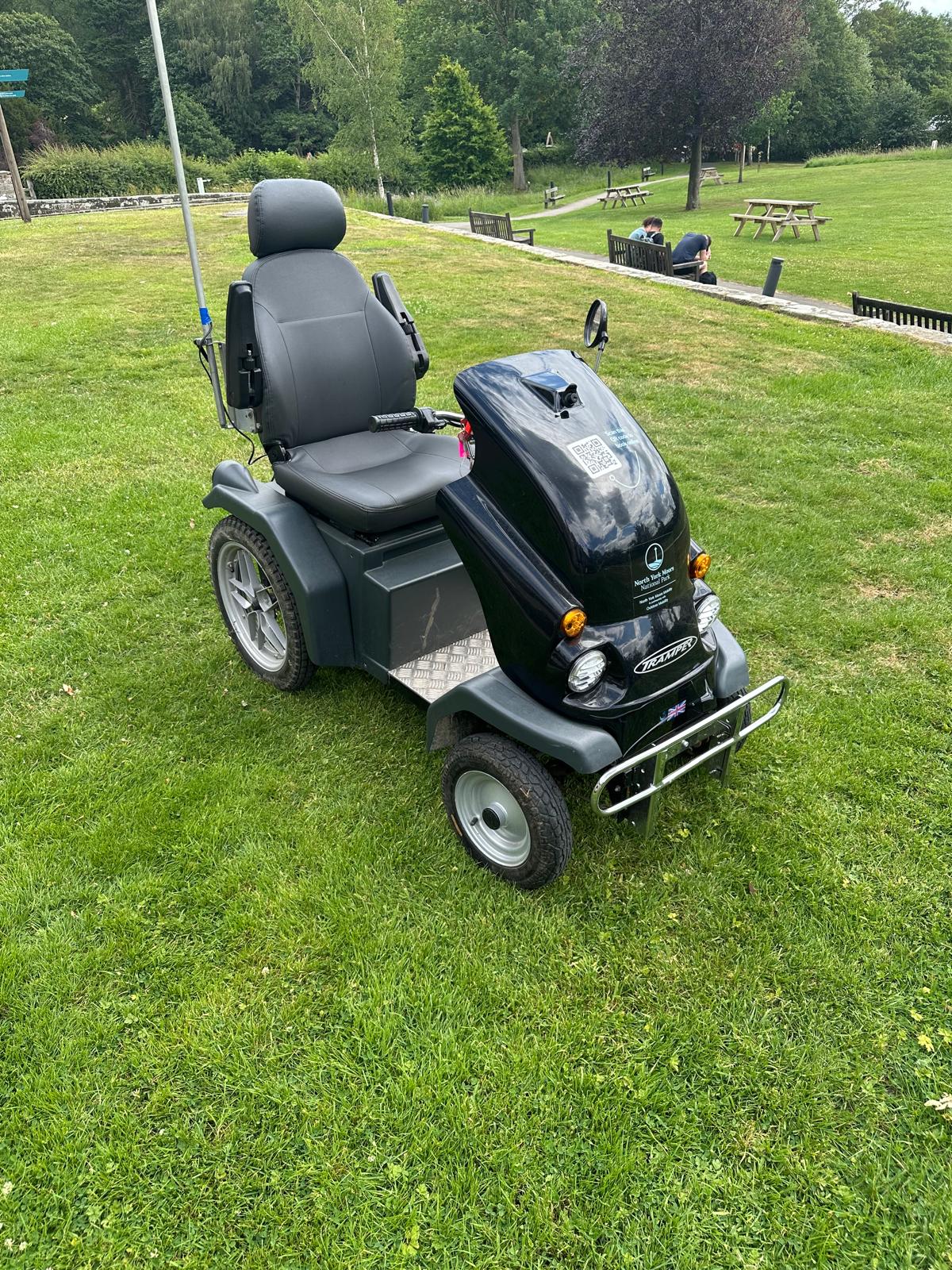 A black Tramper all-terrain mobility scooter parked on grass at the National Park Centre, with picnic tables behind