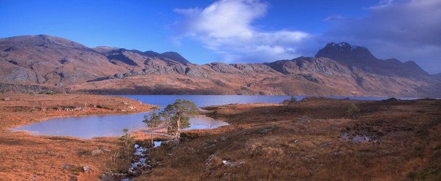 Sunset casting golden hues over the western hills by Loch Arkaig, with the calm waters reflecting the vibrant sky.