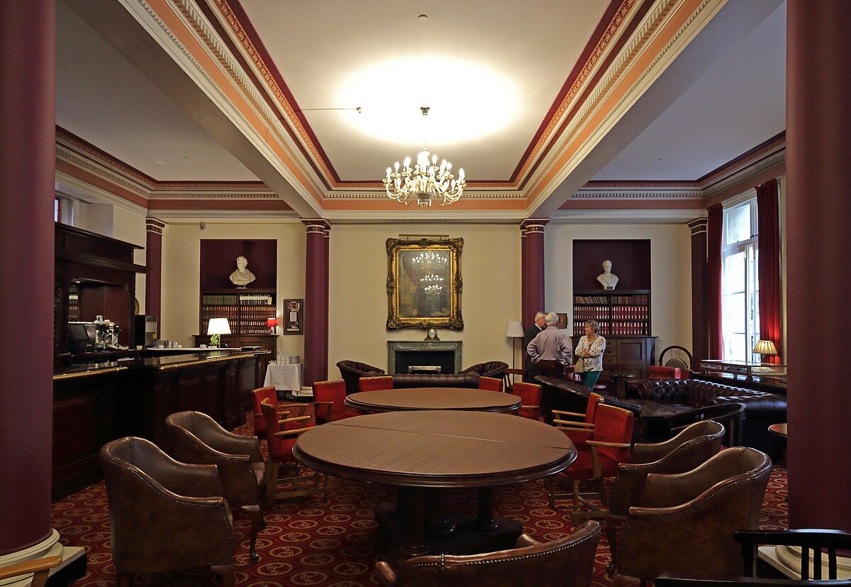 Traditional members’ lounge at the Liverpool Athenaeum with round tables, leather chairs, bookshelves and classical busts.